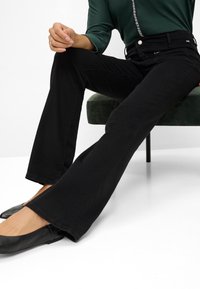 Jeans neri a zampa d'elefante realizzati in denim, con vita alta, cinque tasche e una leggera elasticità. Abbinati a ballerine nere.