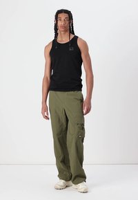 Μαύρο αμάνικο τοπ με μικρό λογότυπο, σε συνδυασμό με φαρδιά ελαιοπράσινα cargo παντελόνια που διαθέτουν πλαϊνές τσέπες. Το μοντέλο στέκεται σε απλό φόντο.