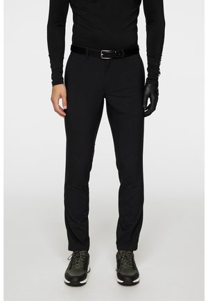Svarta, slim-fit byxor tillverkade av lättviktig tyg, med slät front och bälteshällor. Kombineras med mörka sportskor.