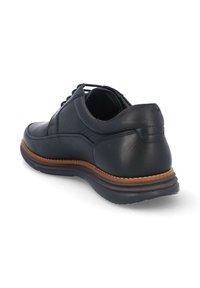 Zapato de vestir negro de cuero con un acabado liso, diseño de cordones, entresuela en contraste color marrón claro y tacón redondeado. Presenta detalles de costura mínimos.