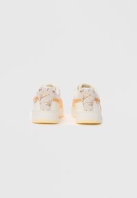 Pantofi sport cu un design floral crem și portocalie deschis, având o textură netedă, guler căptușit și talpă groasă albă și galbenă.