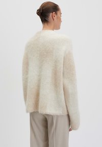 Oversized, cream sweater made of soft, fluffy material with a subtle beige gradient. Features long sleeves and a straight back hem.