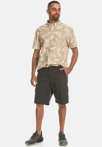 Short-sleeve beige button-up shirt with white floral pattern, paired with dark shorts featuring cargo pockets and black athletic shoes.