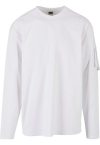 Balta ilga rankovė t-shirt marškinėliai, pagaminti iš minkštos medžiagos, su apvaliu iškirpimu ir užtrauktuku užsegama kišene kairėje rankovėje.