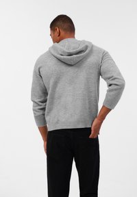 Grijze gebreide hoodie met een achternaaddetail, voorzien van een trekkoordcapuchon en driekwartmouwen, gedragen met zwarte jeans.