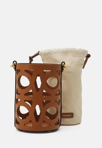Brown cut-out design handbag with a beige fabric drawstring bag inside. Features gold hardware accents and a logo tag on the side.
