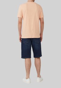 Korte mouwen, perzikkleurig katoenen t-shirt, gecombineerd met donkerblauwe denim shorts met achterzakken en een rechte snit; gedragen met witte sneakers.