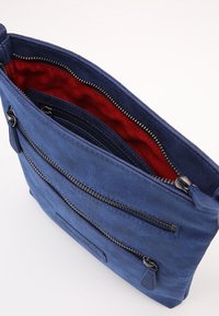 Modrá semišová taška s červenou látkovou podšívkou a několika kapsami na zip. Má kovové zipy a texturovaný vnější povrch.
