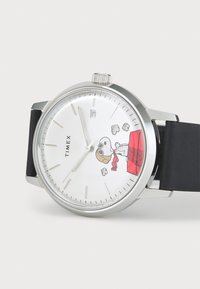 Round silver Timex watch with black leather strap, white dial featuring Snoopy in pilot gear on a red doghouse, and a date window at 3 o'clock.