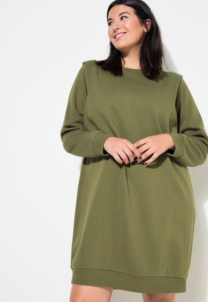 Vestido sudadera verde oliva con corte holgado, escote redondo y puños acanalados. Presenta detalles en los hombros y un dobladillo recto.