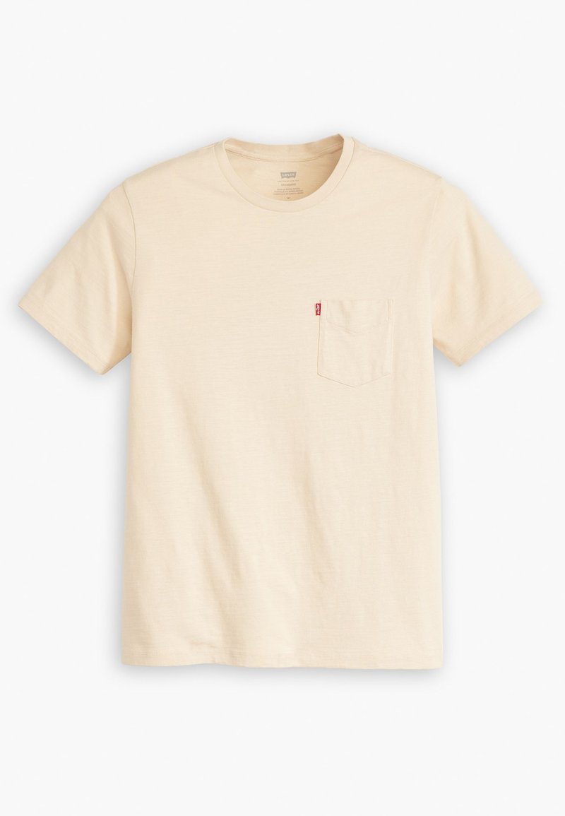 T-shirt en coton beige clair avec un col rond, des manches courtes et une petite poche sur la poitrine gauche. Présente une étiquette de logo rouge sur la poche.