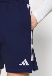 Marineblauwe sportshorts met witte zijstrepen, gemaakt van zachte stof. Voorzien van een elastische tailleband en een klein geborduurd logo aan de zoom.