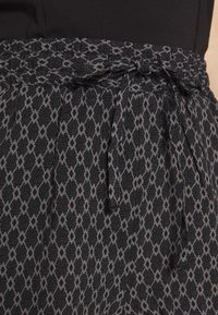 Černá sukně s vzorem a šedým diamantovým designem. Elastický pas s mašlí. Lehká, texturovaná tkanina.