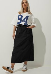 Svart maxiklänning med fickor, med en snörning i midjan. Matcher en vit oversized t-shirt som har en blå "94" grafisk design.