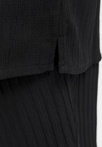 Tejido negro texturizado con rayas verticales y una ligera abertura en el dobladillo, que muestra un diseño ligero y fluido. Acabado suave y caída blanda.