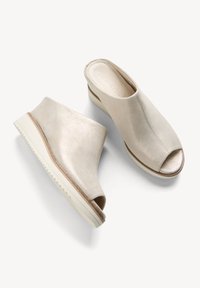 Zapatos abiertos de ante beige claro, con una superficie texturizada, que presentan una suela cuña blanca y un sutil acento alrededor de la abertura.