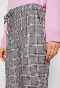 Gray plaid trousers with pink accents, featuring a drawstring waistband and a side pocket with a zipper. Textured fabric.