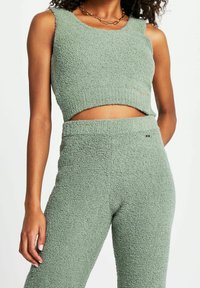 Top cropped verde in un materiale texturizzato e fuzzy, abbinato a pantaloni a vita alta coordinati, entrambi con una finitura morbida e accogliente.