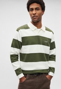 Rohelist ja valget triibulist pika varrukaga polosärki, millel on krae. Valmistatud puuvillast, vasakul rinnal tikitud logo. Vabaaja lõige.