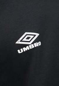 Black fabric with a white Umbro logo featuring two overlapping diamonds and the brand name beneath, slightly worn in texture.