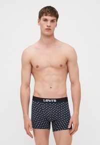 Moške bokserice z črnim pasom z oznako "Levi's", ki imajo temno modro blago z vzorcem in geometrijskimi oblikami v beli barvi.