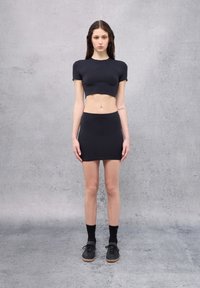 Crop top nero e mini gonna realizzati in tessuto liscio. L'outfit presenta un design aderente con maniche corte e vita alta. Calzature nere completano il look.