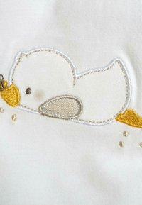 Design di un'anatra ricamato su tessuto bianco, con becco e zampe gialli, contorni grigi e dettagli di texture sottili con piccoli accenti gialli.