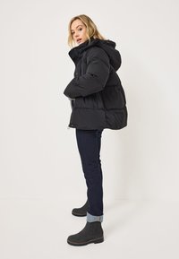 Chaqueta acolchada negra con capucha, con textura acolchada y puños elásticos. Combinada con jeans de mezclilla oscura y botas negras de tobillo.