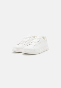 Baskets blanches en cuir avec une texture lisse, bout rond et semelle en caoutchouc plate. Présente un laçage avec six œillets et un branding subtil.