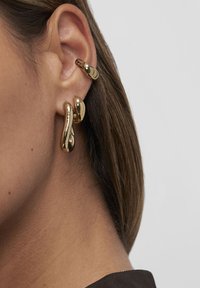 Nahaufnahme eines Ohrs mit drei glänzenden goldenen Ohrhängern, zwei am Ohrläppchen und einer am oberen Ohrknorpel, getragen mit glattem Haar.