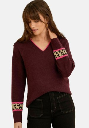Maglione bordeaux a scollo a V con bordi rosa e motivo leopardato sui polsini. Texture morbida e vestibilità rilassata. Abbinato a jeans neri a vita alta.