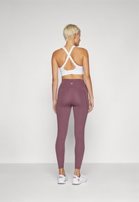 Fehér sportmelltartó, keresztpántos hátrésszel, fitted bordó leggingszel párosítva. Simább textúra, logó részlettel a derékpánton. Fehér sportcipők.