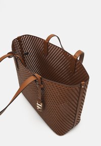 Bruine geweven draagtas gemaakt van flexibele materialen met leren accenten. Bevat twee stevige schouderbanden en een decoratieve gouden gesp.