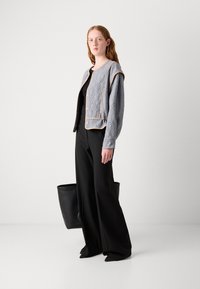 Grijze gewatteerde vest met contrasterende piping, voorzien van knoopsluitingen en een ontspannen pasvorm, gecombineerd met zwarte wijde broek en een zwarte tas.