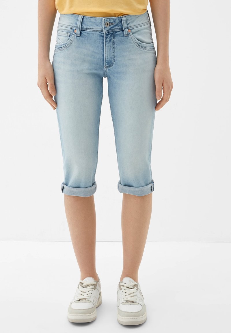 Vaqueros capri de mezclilla de color azul claro con dobladillos enrollados, cinco bolsillos y un diseño ajustado, complementados con zapatillas blancas.