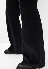 Zwarte corduroy wijde broek met een structuur, voorzien van een hoge taille en contrasterende zwarte chunky laarzen zichtbaar aan de onderkant.