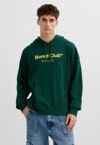 Sudadera con capucha verde hecha de una tela suave que presenta un gran logo y texto amarillo "Bored Club™". Incluye un bolsillo frontal y una capucha con cordón.