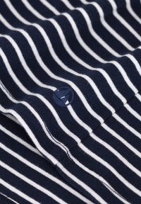 Navy en witte gestreepte stof met een zachte textuur, met een ronde logo-accent in de onderste hoek. Ontworpen als een close-up weergave.