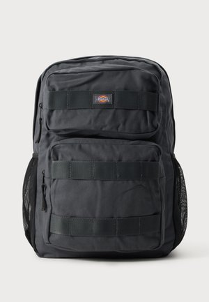 Mochila negra Dickies con dos bolsillos frontales con cremallera, bolsillos laterales de malla y detalles de correas horizontales sobre un fondo liso.