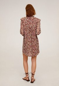 Abito a stampa floreale con maniche corte e volant, vestibilità comoda e una texture leggermente trasparente. Gli accessori includono sandali in pelle marrone con lacci.