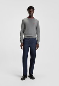 Gray knitted sweater with red collar detail, paired with dark blue pants. Simple design, straight fit, and smooth texture. Black shoes.