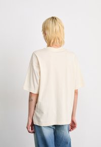 T-shirt en coton surdimensionné couleur crème avec manches courtes, présentant un col rond et une texture lisse, vue de dos.
