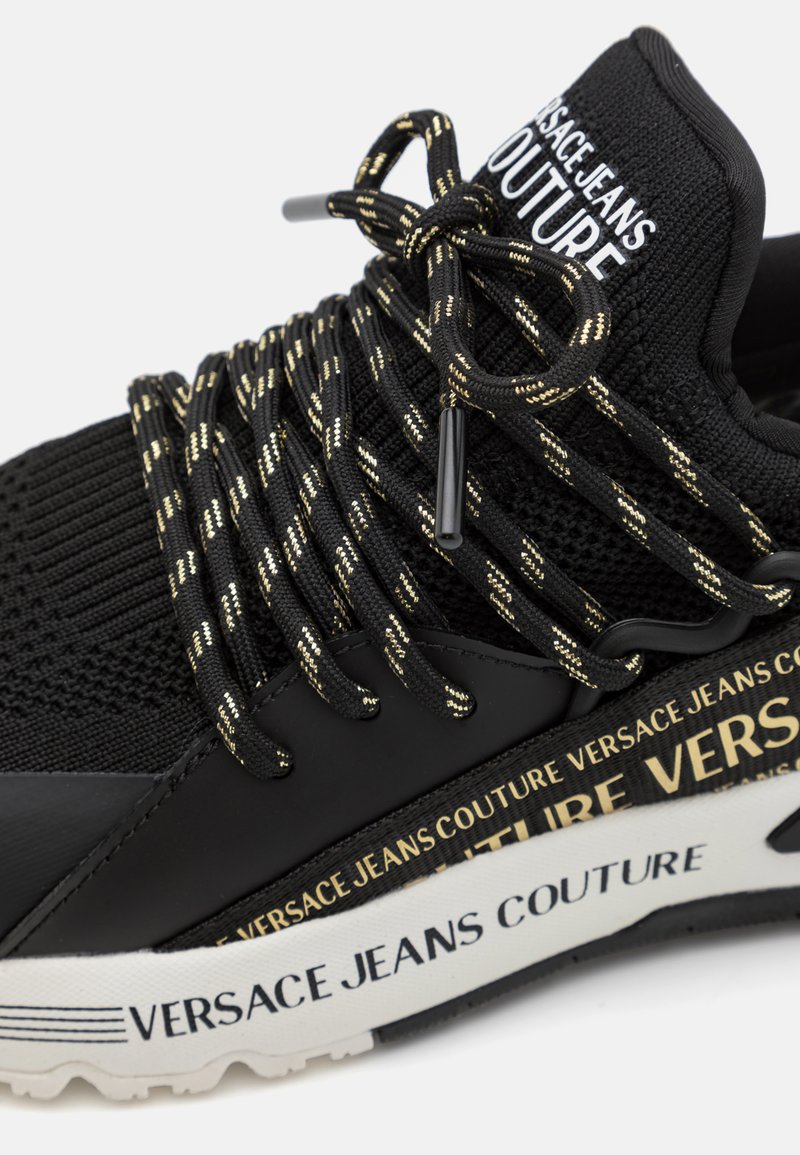 Czarne sneakersy z teksturowanym górnym materiałem z dzianiny, grubą gumową podeszwą, sznurówkami z akcentami w kolorze złotym oraz detalami brandingowymi na boku.