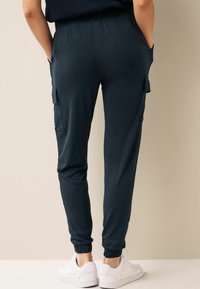Navyblauwe taps toelopende joggers met een elastische tailleband, zijzakken en gebandeerde enkels, gecombineerd met witte sneakers. Gladde stofstructuur.