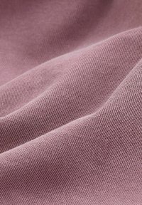 Nahaufnahme eines weichen, strukturierten, roséfarbenen Stoffs mit sichtbarem Strickmuster und sanften Falten, die Tiefe und Schatten erzeugen.