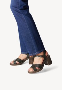 Zwarte leren sandaaltjes met hak en gekruiste banden met een enkelgesp, met een gestructureerde afwerking. Gepaard met blauwe wijde jeans.