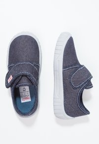 Denim slip-on sko i mørkeblå med hvite sømmer og gummisåler. Har en borrelås for enkel påsetting.