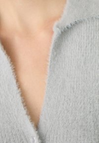 Cardigan grigio chiaro morbido e peloso con scollatura a V profonda, che mostra la pelle nuda sottostante.