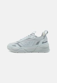 Gray athletic sneaker with a smooth synthetic upper, rubber sole, textured accents, and reflective logo detail. Lace-up closure with pull tab.