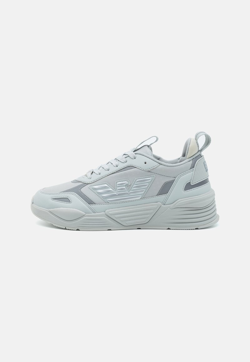 Gray athletic sneaker with a smooth synthetic upper, rubber sole, textured accents, and reflective logo detail. Lace-up closure with pull tab.